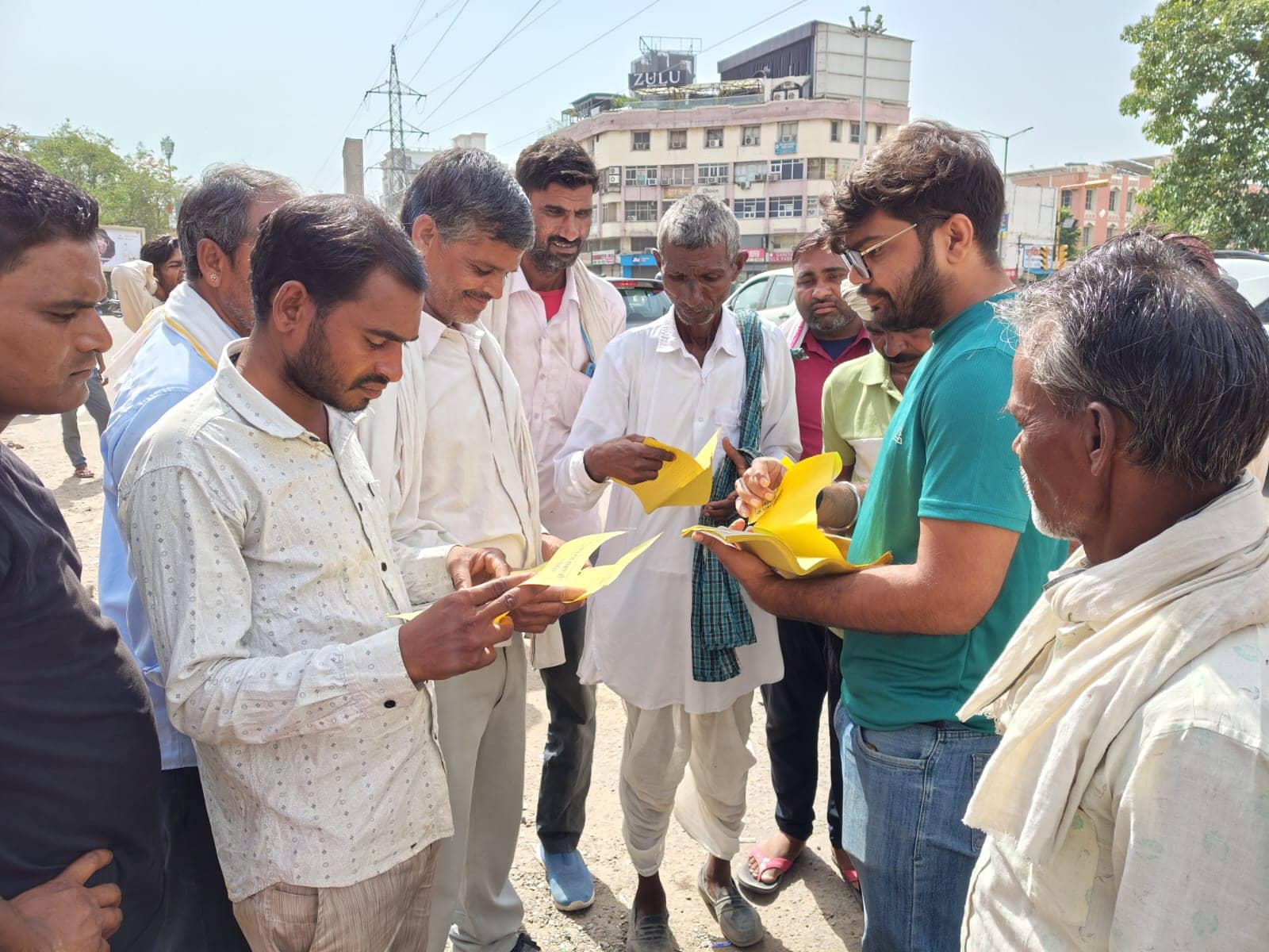 A volunteer in a green T-shirt hands yellow information leaflets to a group of men, who read them closely, on a city street.